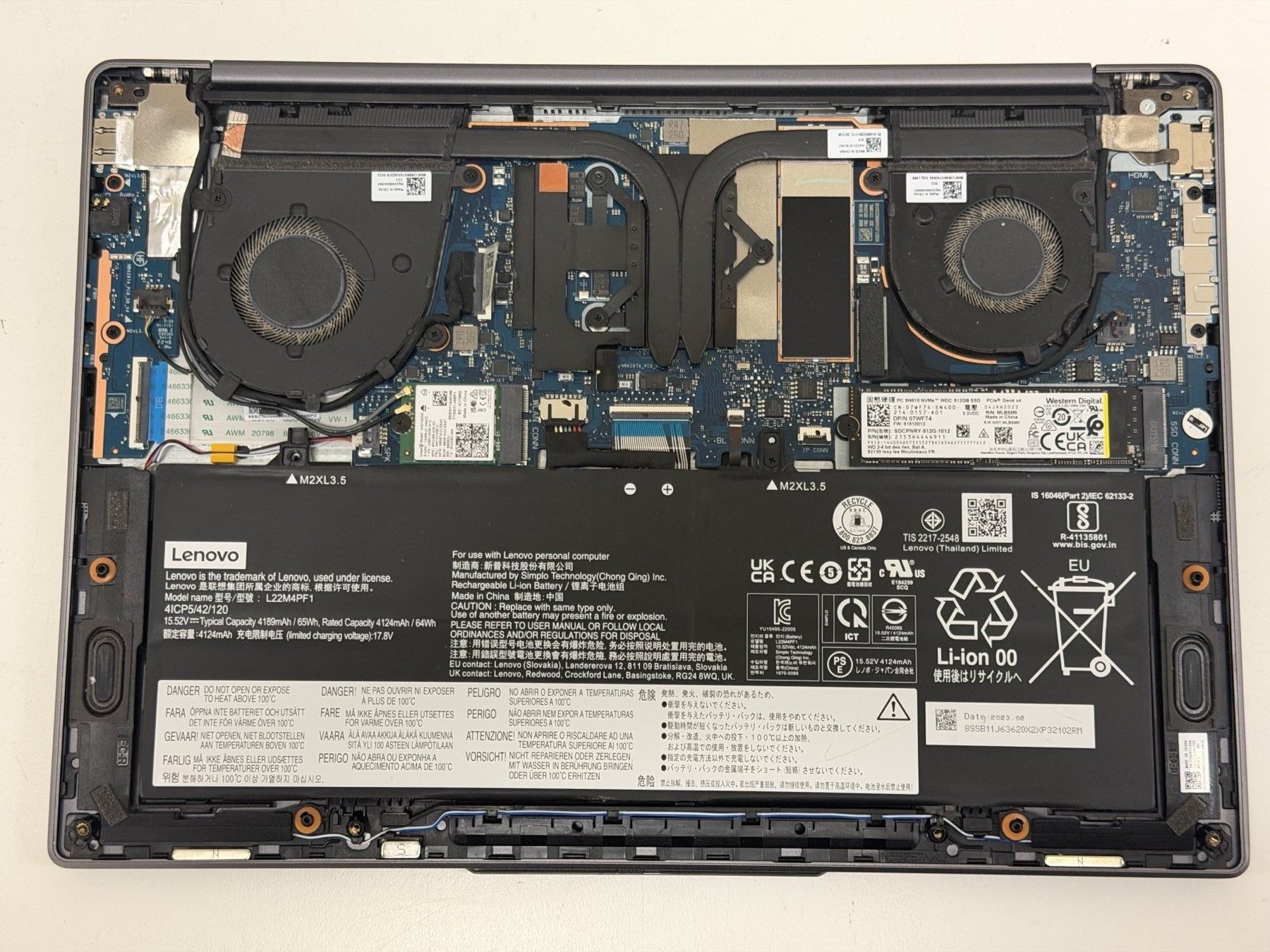 A Lenovo laptop with the bottom cover removed on our Perth workshop bench, showing the dual cooling fans, copper heatpipe, M.2 SSD slots and Lenovo Li-ion battery — representing the thermal repair, fan replacement, repaste and board-level work we do on Lenovo laptops including the Legion gaming range.